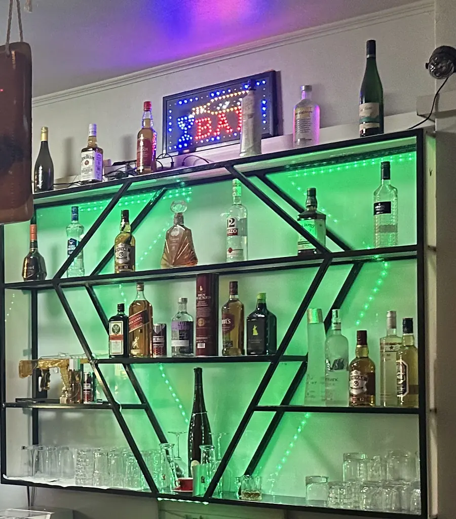 Grün beleuchtetes Flaschenregal hinter der Theke mit Whisky, Wodka und Ouzo